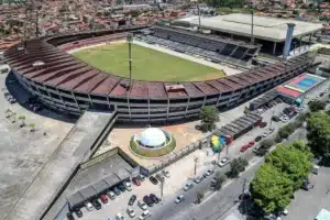 Vista aérea do Estádio Rei Pelé em Maceió, com o campo de futebol e as arquibancadas, sob um céu claro.