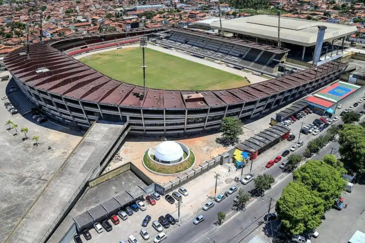 Vista aérea do Estádio Rei Pelé em Maceió, com o campo de futebol e as arquibancadas, sob um céu claro.