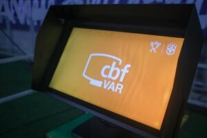 Sistema VAR sendo utilizado em partida de futebol com árbitros analisando lance polêmico